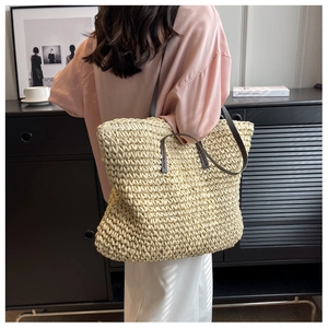 Large woven straw tote bag with brown leather handles shown on shoulder for daily commute