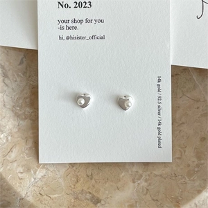 Close-up of minimalist heart-shaped silver earrings with elegant round white pearls