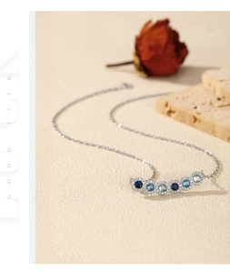 Detail of S925 silver necklace with gradient blue round crystals on a warm textured background