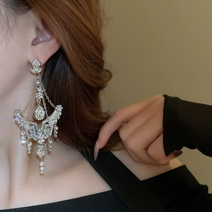 Macro detail of oversized silver drop earrings with shimmering crystals and tassels