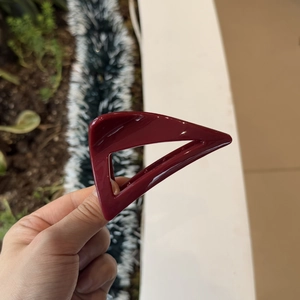 Detail shot of a glossy burgundy triangular hair claw clip held against a natural background