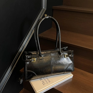 Glossy black PU leather tote bag with gold buckle on wooden stairs with book