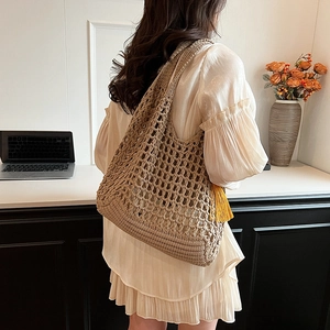 Beige handwoven hollow knit tote bag with yellow tassel on a casual office desk