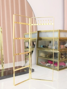 Golden folding jewelry organizer rack on a desk with multiple holes for earring display