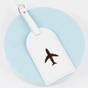 Detail of white leather luggage tag featuring an embossed bronze airplane design