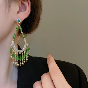 Vue macro de boucles d'oreilles fleur avec perles vertes et pompons sur un modèle