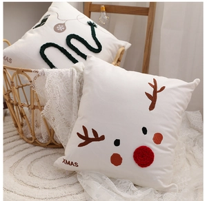 Detail of Christmas throw pillows with reindeer embroidery and XMAS text in a cozy basket