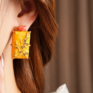 Gros plan d'une boucle d'oreille carrée vintage en émail orange avec perle rouge et prune d'or