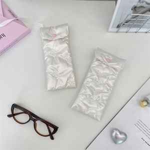 Detailed view of cream PU leather padded sunglasses pouches with heart embroidery and bow