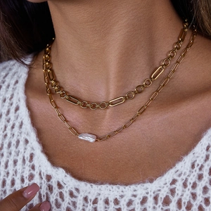 Detail van gelaagde gouden paperclip ketting met een barokke zoetwaterparel bij een model