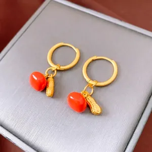 Chinese style gold earrings featuring red persimmon beads and peanut pendants on a jewelry box