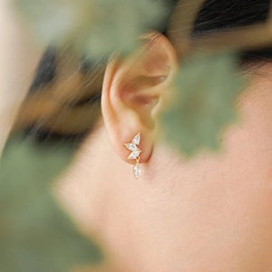 Elegant gold stud earrings with leaf-shaped marquise zircons worn by a model in nature