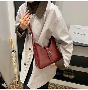 Gros plan d'un sac bandoulière bordeaux avec boucle métal sur un mannequin en manteau beige