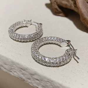 Dettaglio macro di orecchini a U in rame argento con zirconi pavé e motivo a rombi