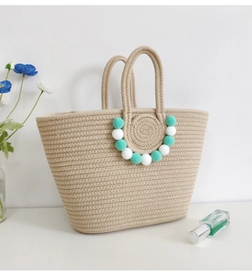 Detail of handmade straw tote bag with decorative white and turquoise pom-pom charms