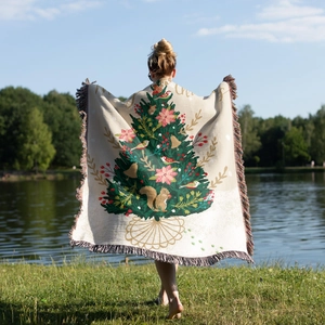 Outdoor view of a woven Christmas tree blanket with fringes and festive illustration