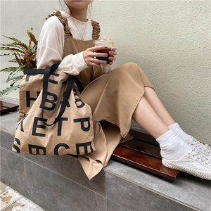 Outdoor model shot of a large canvas tote bag in light brown with black letter printing