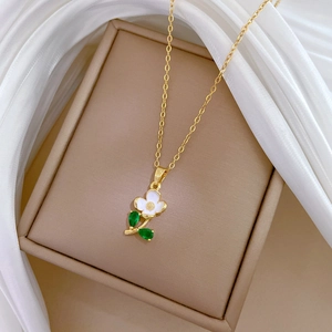 Elegant gold titanium necklace with white flower and green leaf pendant on jewelry box