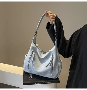 Close-up of light blue soft leather tote bag showing grainy texture and fringe zippers
