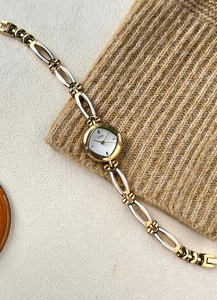 Elegant gold-tone bracelet watch with white enamel inlay on a textured background
