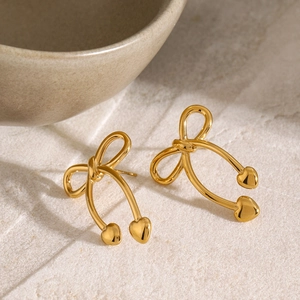 Detail of gold bow earrings with heart pendants on a textured natural stone background