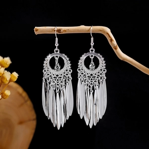 Detailed view of silver ethnic leaf tassel earrings hanging on a natural wooden branch