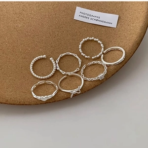 Set of seven minimalist silver rings featuring twist, heart, and chain designs on cork