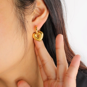 Close-up of elegant gold heart-shaped dangle earring worn by a model on white background