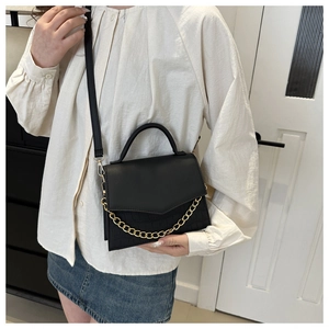 Detail of black faux leather crossbody bag with crocodile texture and gold chain link