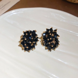 Macro shot of irregular black crystal stud earrings with gold accents on white ceramic