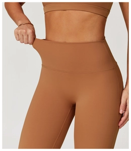 Detail der hochelastischen Taille der karamellbraunen Yoga-Leggings beim Dehnen des Stoffes