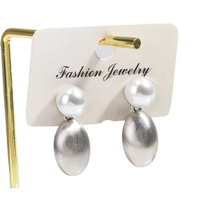 Elegant pearl earrings with brushed silver oval pendants on a white jewelry display card