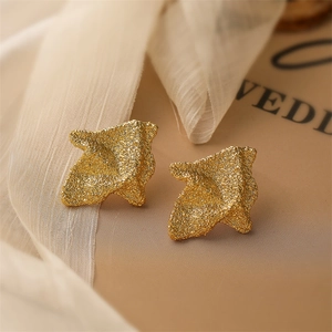 Macro detail of golden teardrop earrings with frosted texture and irregular pleated finish