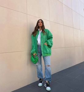 Fashionable street style showing bright green bomber jacket and ripped blue denim jeans