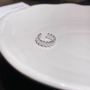 Close-up of a silver gear-textured ear cuff on a white ceramic plate with soft light