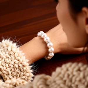 Close-up of white pearls and zircon flower charm on a model's wrist with knit sweater