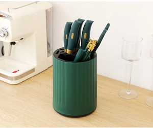 Detail of dark green rotating knife block with gold-rimmed kitchen utensils on wood table