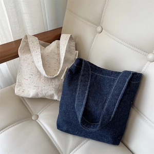 Close-up of confetti denim tote bags in cream and navy blue on a beige leather sofa