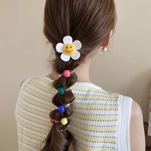 Détail d'une pince à cheveux fleur blanche avec smiley et élastiques à perles colorées