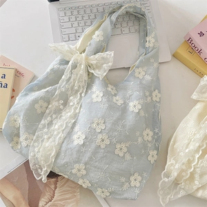 Detailed close-up of light blue floral embroidery and lace bow on a canvas tote bag