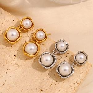 Detail view of 18K gold and silver plated square pearl earrings on beige stone base