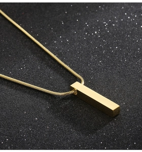 Detailed close-up of golden square column pendant with snake chain on dark background