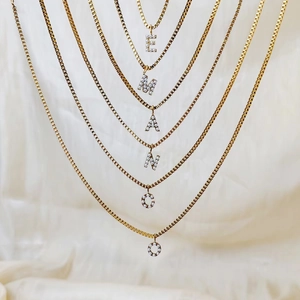 Close-up of gold titanium steel box chains with pearl-encrusted letter pendants