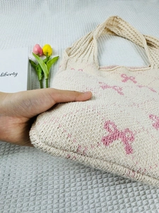 Close-up of knit tote bag showing soft cream texture and pink bow pattern detail