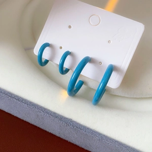 Detailed close-up of glossy blue C-shaped enamel earrings on a white jewelry card display