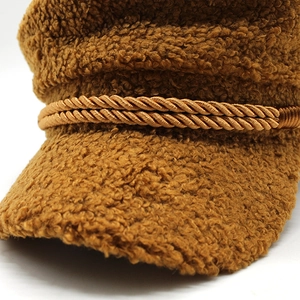 Detail of a brown newsboy cap in lamb wool featuring a gold braided decorative cord