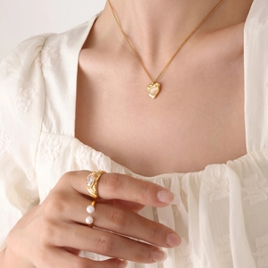 Luxury gold heart pendant necklace and pearl ring set shown on model in a warm tone