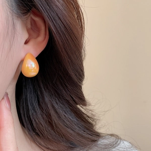 Macro view of teardrop iridescent orange acrylic stud earring worn on model ear