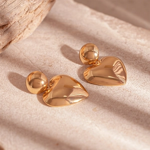 Detailed view of gold geometric stud earrings with polished heart charms on a stone surface