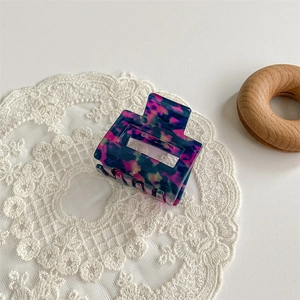 Detailed close-up of a square multi-colored acetate hair claw on white lace fabric